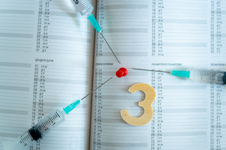Third covid vaccine dose and jab concept. Three syringes are seen on calendar as a concept for the 3rd covid-19 vaccine dose, also called booster shot, now requested during the vaccination campaign.の写真素材