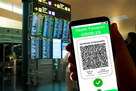 A Covid certificate, also called covid passport, is seen on the screen of a mobile phone with an airport in the background. More and more countries are adopting the Covid19 vaccination passportのeditorial素材
