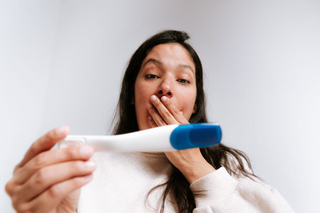 young adult woman looking at pregnancy test with happy expression in her bedroom. latina woman with...