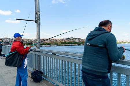 Istanbul, Turkey - 10 May 2023: fishermen are seen fishing with their fishing rod over the iconic...