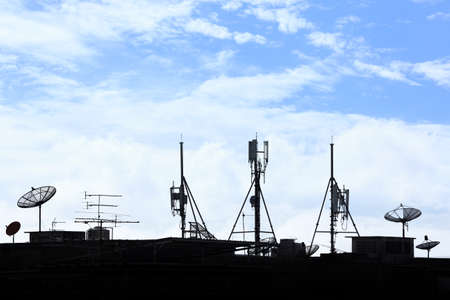 Silhouette various communication devices on rooftop; cell site, satellite receiver, TV antennaの写真素材