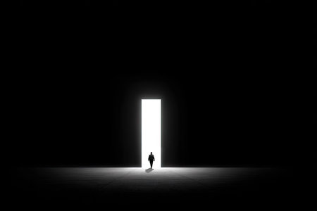 Person walks toward a brightly lit doorway in a dark space. The image uses a stark contrast of light and shadow to create a dramatic and minimalist atmosphere.  The focus is on the journey and the sense of hope and possibility implied by the light.の素材