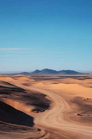 A desert scene showing a winding dirt road cutting through rolling sand dunes beneath a blue sky.の素材