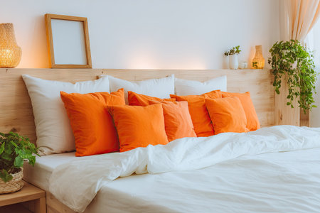 Comfortable bedroom interior showcasing a wooden headboard, a stack of orange throw pillows, and white bedding.  The room has a calming and inviting atmosphere.の素材
