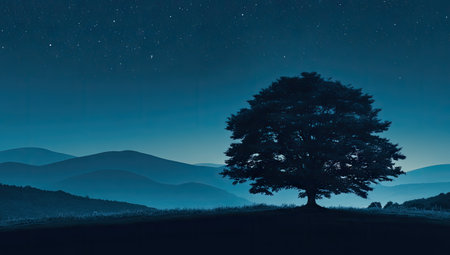 Silhouetted tree stands alone on a hilltop overlooking a misty mountain range bathed in the soft blue light of a starlit night. The image evokes a sense of serenity and quiet contemplation.の素材