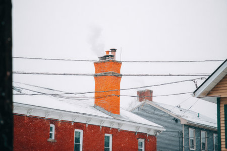 View of a red brick building with an orange chimney, situated on a snowy day, featuring snow-covered roofs and power lines crisscrossing the scene.の素材