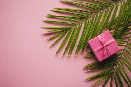 A pink gift box is surrounded by lush green palm fronds on a soft pink backdrop.の素材