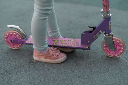 Close up on woman legs feet standing on the electric kick scooter on the pavement wearing jeans and sneakers in summer dayの写真素材