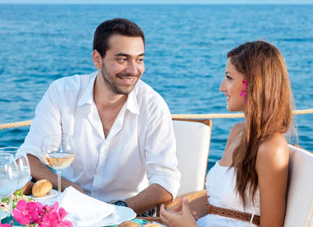 Young couple enjoying a romantic meal sitting at a table at a waterfront restaurant talking to each other with an ocean backdropの写真素材