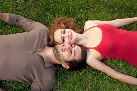 Young couple resting on the grass lying on their backs looking up into the camera