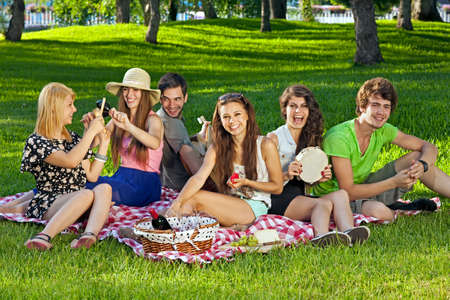 College students enjoying a picnic in the park sitting grouped together on rug on the grass laughing and joking amongst themselvesの写真素材