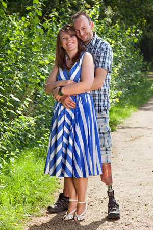 Joyful romantic young couple standing hugging each other on a rural path with a handsome disabled amputee with a prosthetic leg and a stylish young womanの写真素材