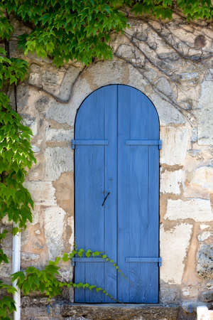 Old narrow door, blue painted in an ancient house block stone wall, surrounded by ivy tendrils  France, Provence の写真素材