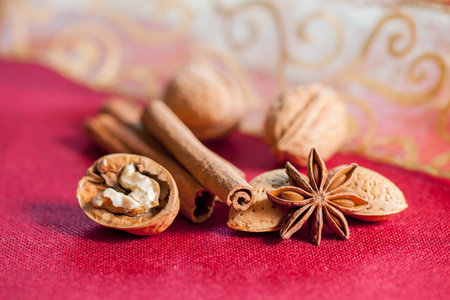Christmas composition on a red table cloth surface. Almonds, cinnamon sticks, star anise, opened...