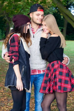 A male student is flirting with two female friends on a warm autumn day in a park.の写真素材