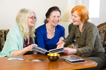 Three Adult Women Friends, Relaxing at the Living Area, Laughing Together While Looking at their Old Photos in an Album.の写真素材