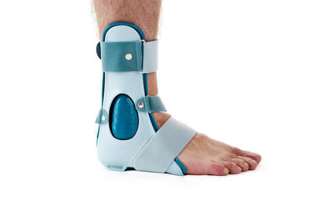 Close Up of Man Wearing Supportive Ankle Cast Brace, Secured by Velcro Straps, in Studio with White Background and Copy Spaceの写真素材