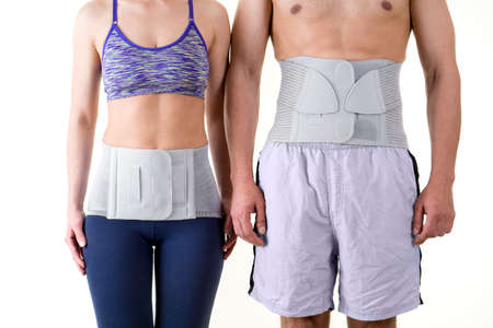 Detail of Mid Section of Athletic Man and Woman Wearing Supportive Orthopedic Back Braces for Lower Back, Standing Together in Studio with White Backgroundの写真素材