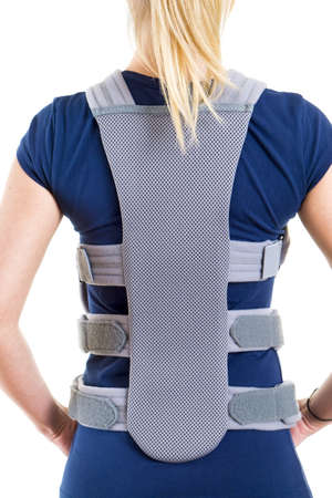Close Up Rear View of Blond Woman in Blue T-Shirt Wearing Padded Back Brace in Studio with White Backgroundの写真素材