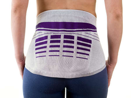 Close Up Rear View of Athletic Woman Wearing Modern Orthopedic Lower Back Brace for Support in Studio with White Backgroundの写真素材