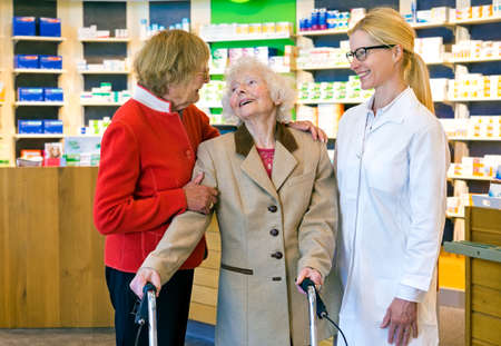 Friendly female pharmacist in pony tail and eyeglasses talking and laughing together in front of pharmacy counterの写真素材