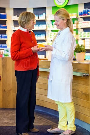 Cheerful female pharmacist handing a senior citizen customer medication product while standing in front of medicine counterの写真素材