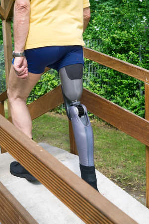 Rear view on single unidentifiable man in blue shorts and yellow shirt walking over concrete and wooden ramp with prosthetic legの写真素材