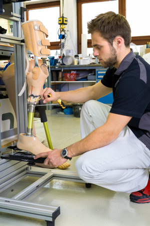 Young bearded man working on shin and knee section on prosthetic leg assembly in laboratory for...