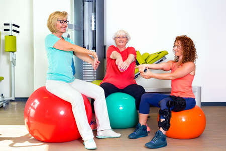 Pair of patients with instructor stretching wrist and forearm muscles while seated on stability balance ballsの写真素材