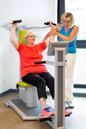Physical therapist helping senior patient with exercises on machine used to increase shoulder strengthの写真素材