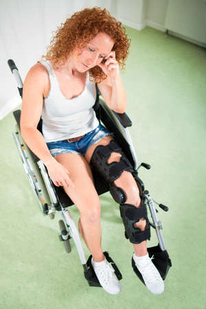 Overhead view of sad woman in leg brace and shorts as she sits in a wheelchairの写真素材