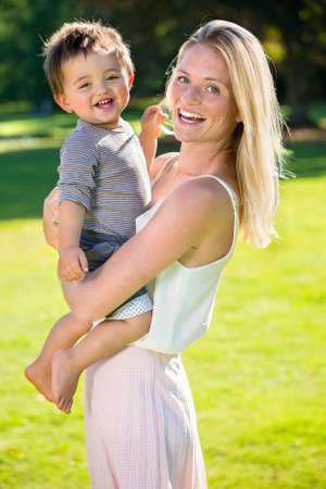 Happy young mother with barefoot male toddler standing together outside on green grassの写真素材