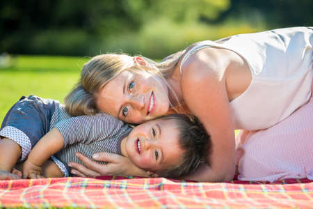 Adorable toddler embraced by happy blond young mother laying down on blanket outsideの写真素材
