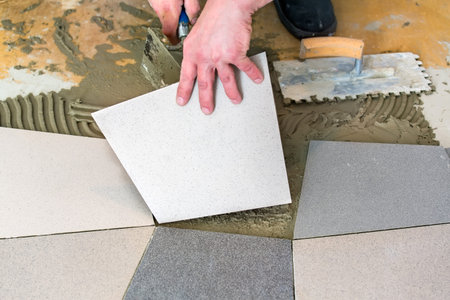 Handyman laying ceramic floor tiles on adhesive using trowel