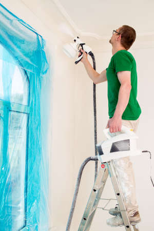Man painting room walls with paint spray gun while standing on ladderの写真素材