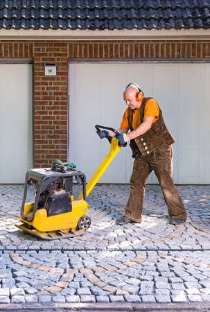 Man using a mechanical compacter on new pavers laid in the driveway entrance to a house during house improvements.の写真素材