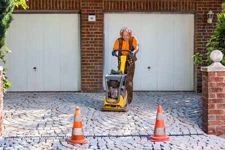 Builder or contractor laying new paving bricks in a house driveway using a mechanical compacter for compaction of the cement pavers.の写真素材