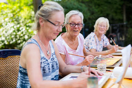 Retired senior women painting together outdoors as group recreational and creative activity during summer.の写真素材