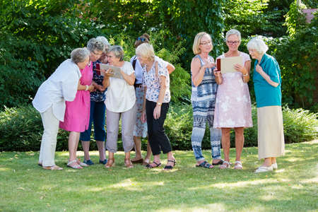 Group of senior women gladly looking at pictures and discussing them, standing in the park after art therapy lesson.の写真素材