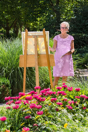 Cheerful senior woman painting in garden on sunny day.の写真素材