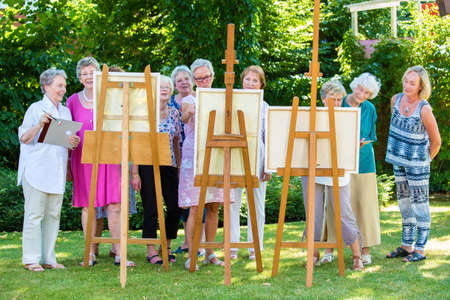 Group of smiling senior women painting on canvas during sunny day in garden.の写真素材