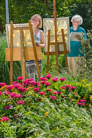 Young and senior cheerful women painting on canvas in garden during sunny day.の写真素材