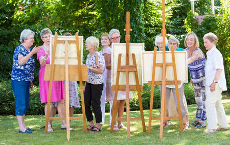 Group of senior ladies enjoying an art class outdoors in a park or garden as a therapeutic recreational activity at a care home.の写真素材