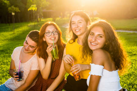 Young and pretty friends with cocktails on sunny summer day in the park having good time. Group lifestyle half-length portrait.の写真素材