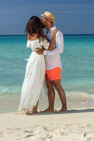 Full length view of a happy couple wearing summer clothes while kissing on a sunny beach during vacations or honeymoon in Cuba.の写真素材