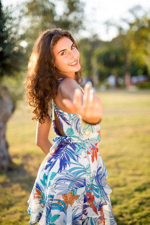 Portrait of happy young woman wearing dress gesturing while standing at park on sunny day.の写真素材