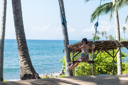Sexy young woman sitting on the swing on the tropical beach, paradise island Bali, Indonesia. Sunny day.の写真素材