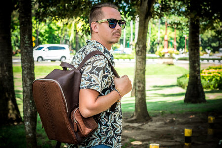 Tourist with stylish brown snakeskin python backpack in the asian park. Bali. Handsome caucasian man...