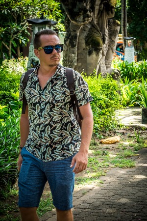 Tourist with stylish brown snakeskin python backpack in the asian park. Bali. Handsome caucasian man in sunglasses.の写真素材