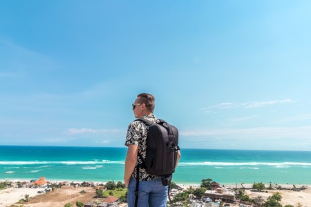 Handsome traveler man stay by blue ocean background - Happy guy relaxing at sea view point - Concept of freedom and summer trip around the world backpacker style. Bali, Indonesia.の写真素材